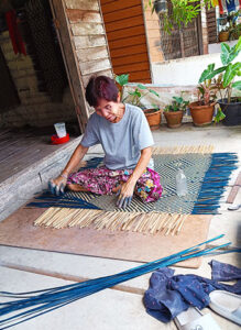 Una mujer tailandesa trenza una estera con materiales naturales en la biorregión de Phatthalung.