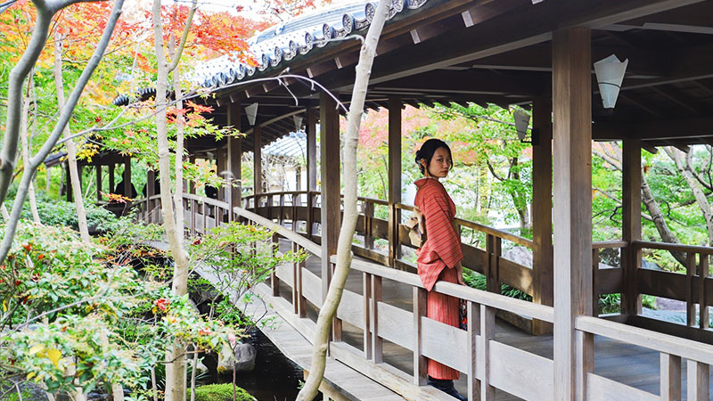 Mujer vestida con yukata caminando por una galería tradicional japonesa rodeada de jardines otoñales