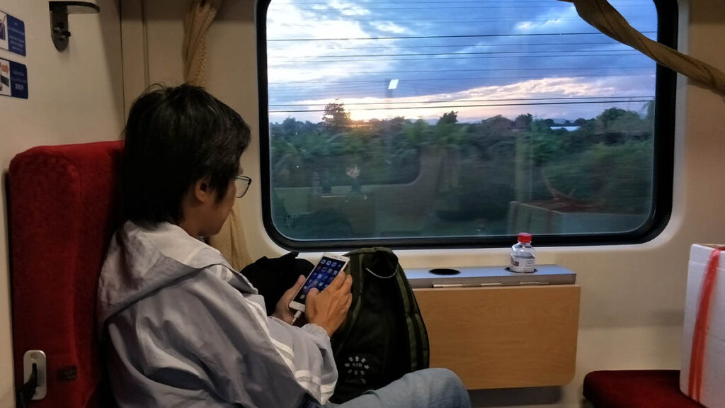 Pasajero a bordo de un tren nocturno en Tailandia observando el paisaje al atardecer
