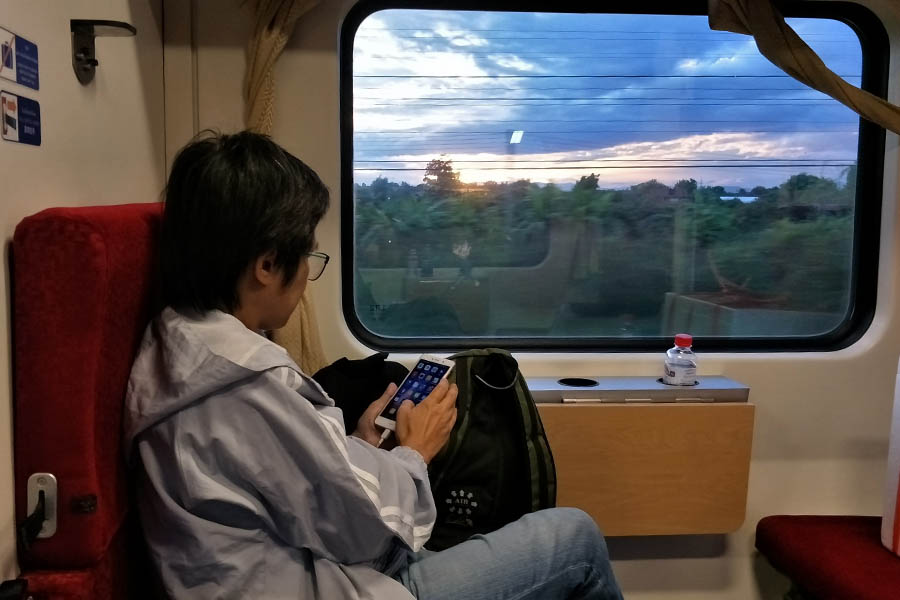Pasajero a bordo de un tren nocturno en Tailandia observando el paisaje al atardecer