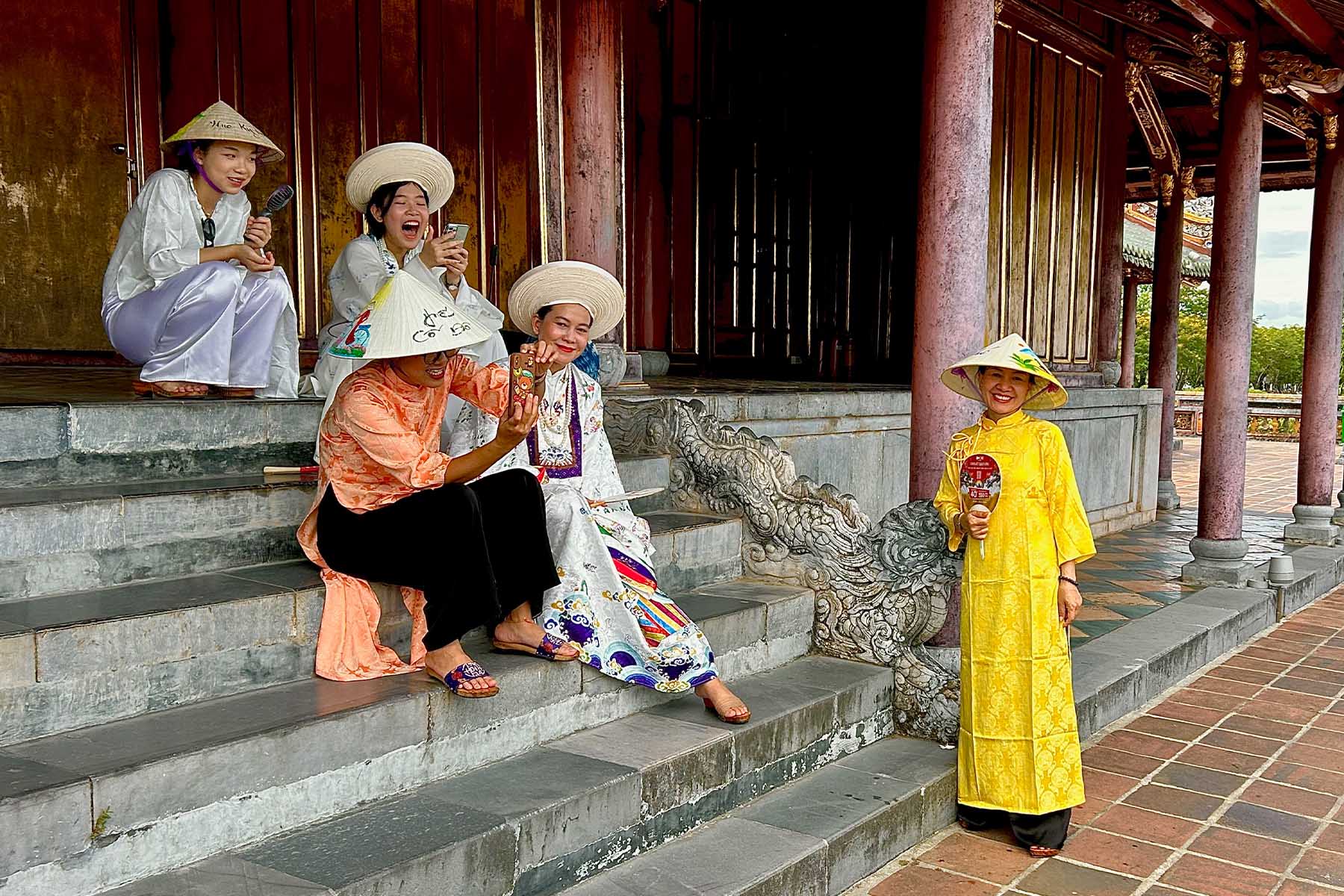 Visitantes con trajes tradicionales vietnamitas sonríen en las escaleras de un pabellón de la Ciudadela Imperial de Hué.