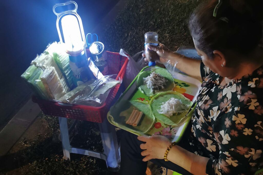 Una vendedora prepara rollitos de pandan bajo una lámpara junto a una avenida de Phnom Penh
